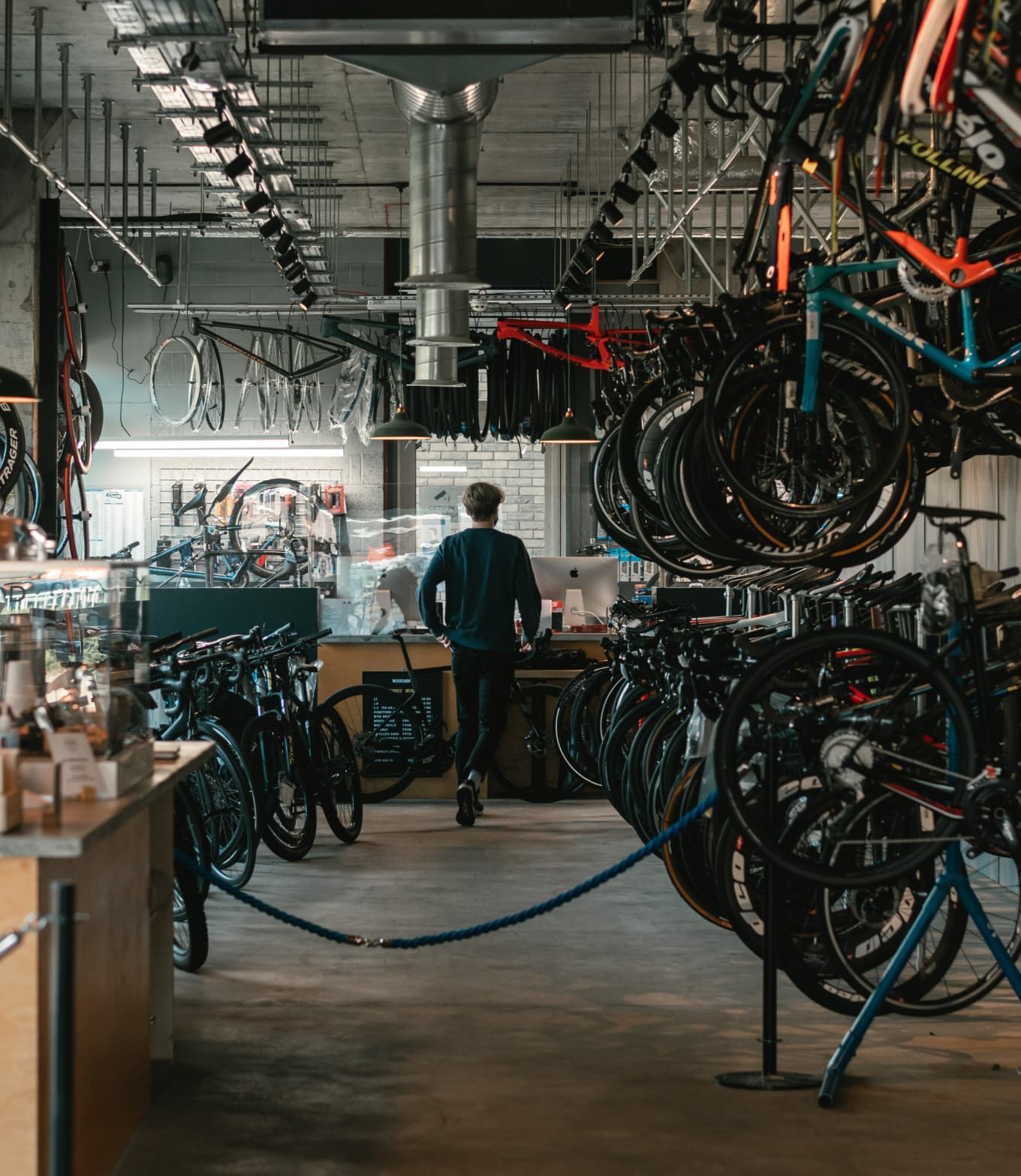 Dentro de uma bicicletaria, com varias bicicletas, peças e uma pessoa no balcão.